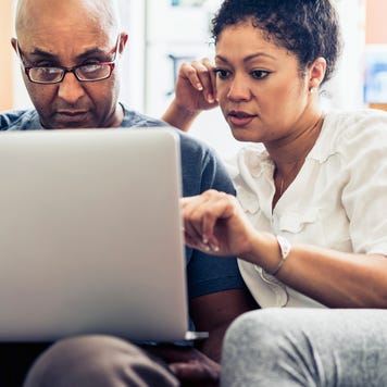 Couple looking at laptop while sitting on sofa at home