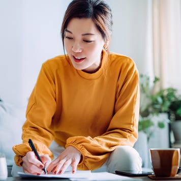 woman holding a pen and signing paperwork in the living room at home