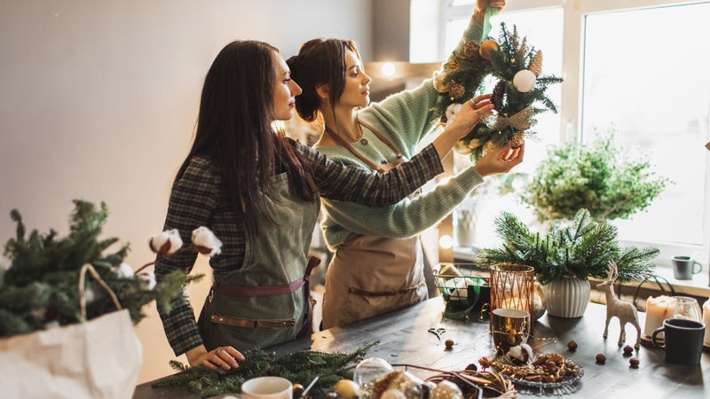 Two women making Christmas wreath using fresh pine branches and festive decorations.