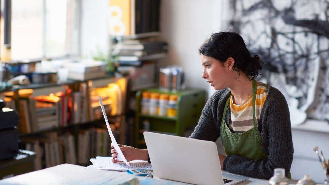 Young female artist in studio working on laptop.
