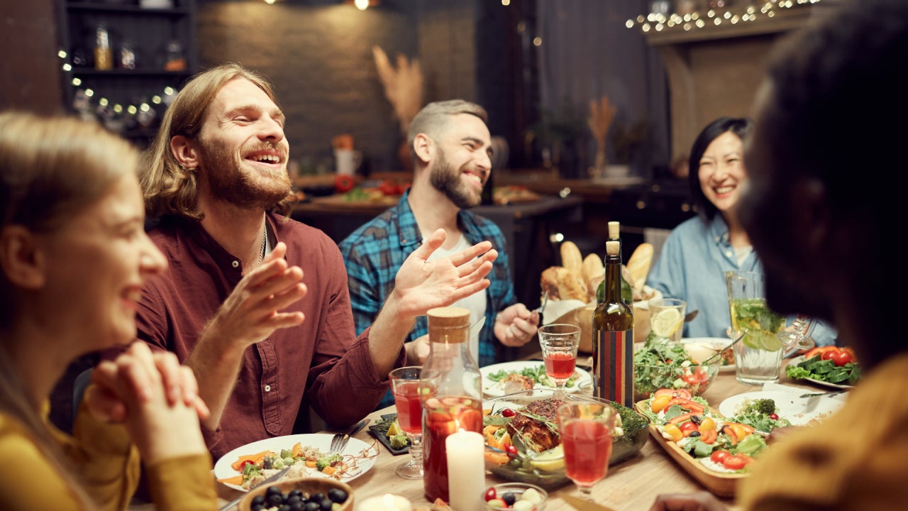 Group of emotional young people enjoying dinner party with friends and smiling happily sitting at table in dimly lit room, copy space
