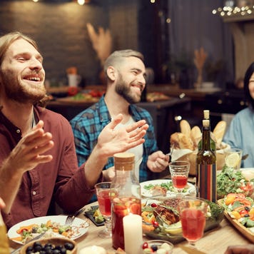 Group of emotional young people enjoying dinner party with friends and smiling happily sitting at table in dimly lit room, copy space
