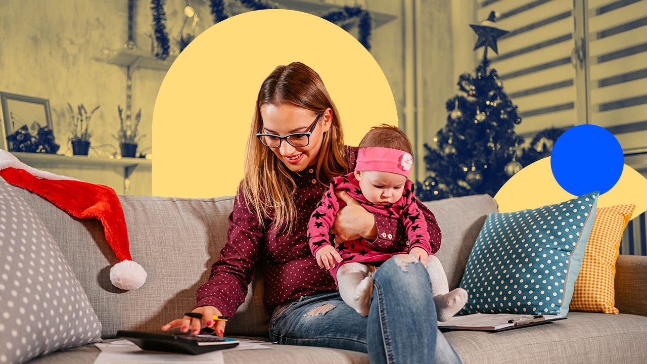 female holding a baby while sitting on a couch using a calculator