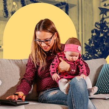 female holding a baby while sitting on a couch using a calculator