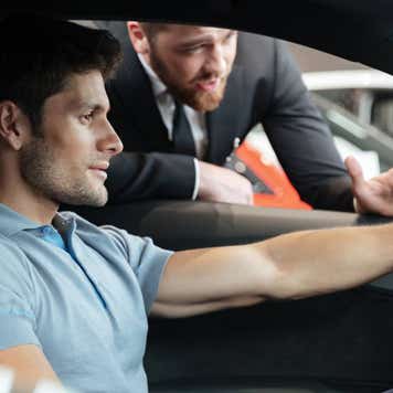 Professional young male dealer selling car to a customer at the dealership