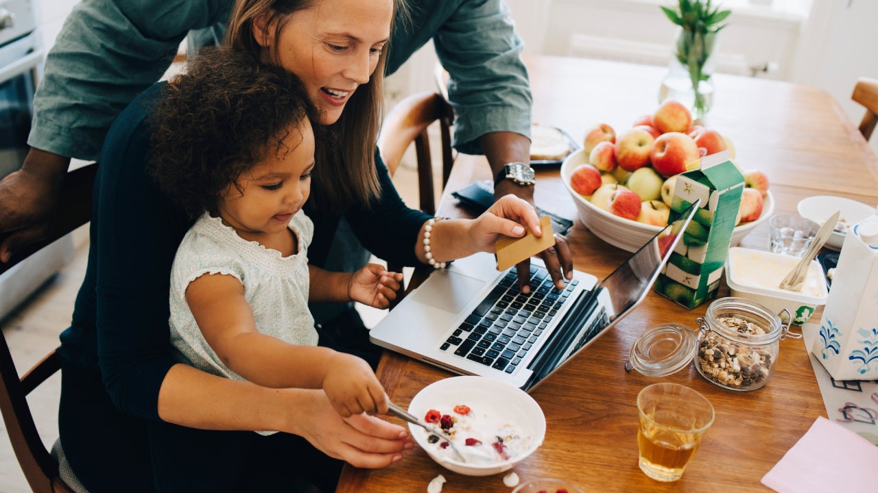 Parents shopping online on laptop while looking at daughter having breakfast in dining room