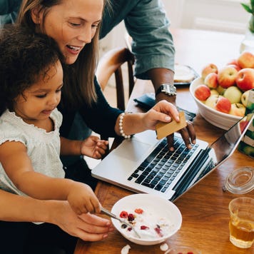 Parents shopping online on laptop while looking at daughter having breakfast in dining room