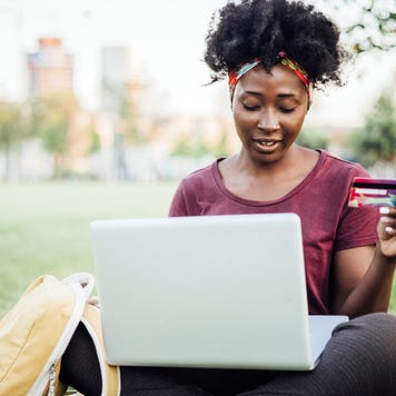 Portrait of a beautiful young African American woman sitting on the grass in the park and shopping online.