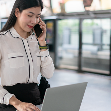 Asian woman on laptop and talking on smartphone
