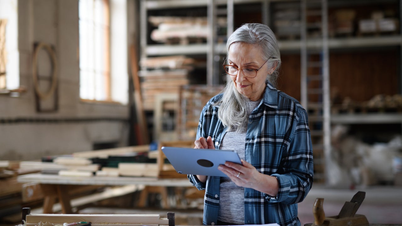 An older woman business owner uses a tablet in a carpentry workshop