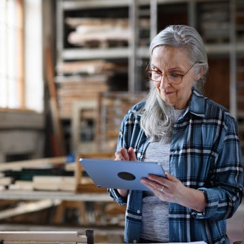 An older woman business owner uses a tablet in a carpentry workshop