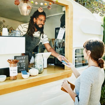 Smiling food truck owner taking credit card for payment from customer - stock photo