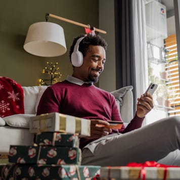 African American man sitting on the floor, using a credit card and smart phone. He is doing online Christmas shopping.