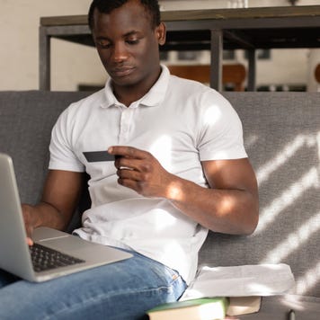 African American student shopping online sitting on sofa - stock photo