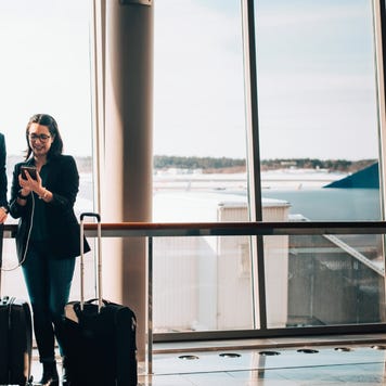 Full length of business couple with luggage using mobile phone in airport