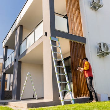 Man painting wooden columns of modern apartment against sky during sunny day