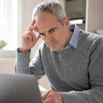Mature caucasian man in his 50s using laptop looking concerned, puzzled and confused.