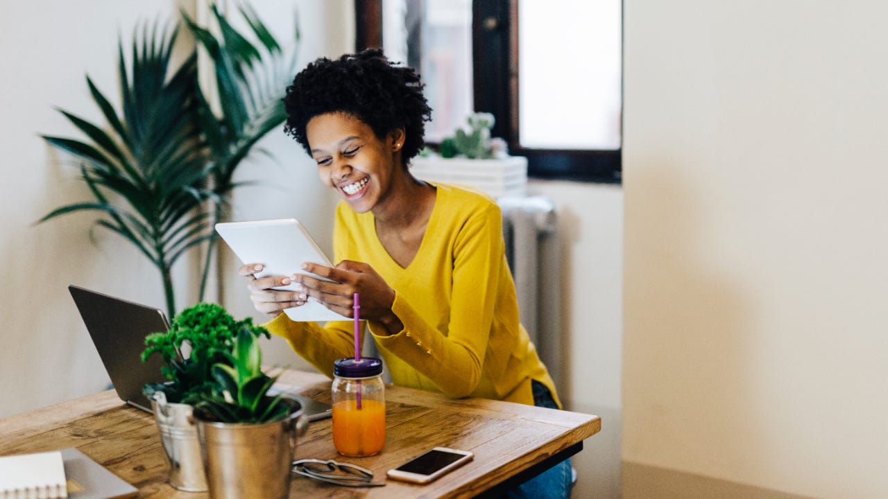 Young Black woman smiling at tablet sitting at a table