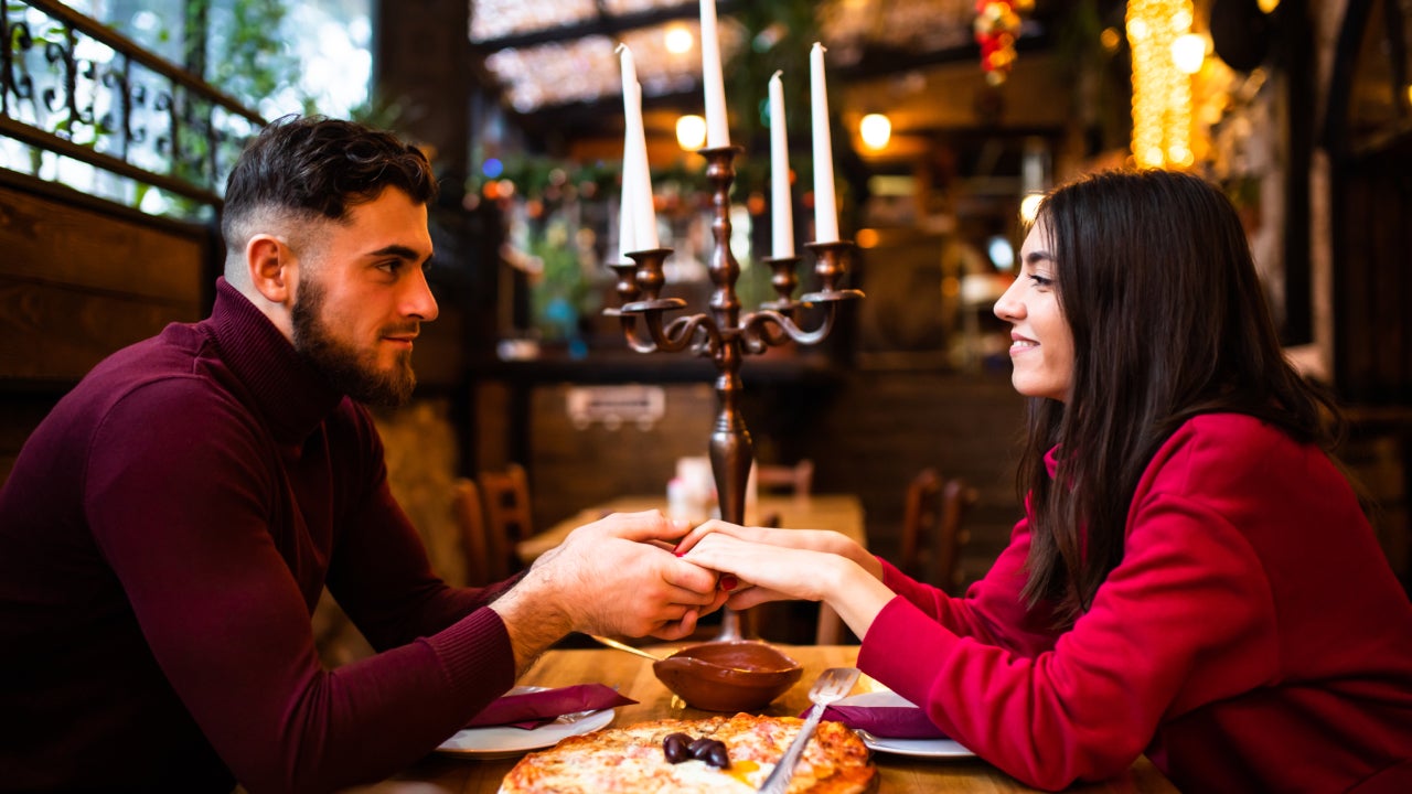 A young couple is holding hands and looking at each other lovingly while at a restaurant on a date on Valentine's Day