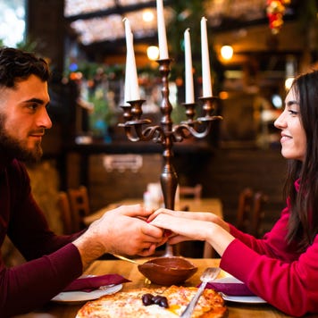 A young couple is holding hands and looking at each other lovingly while at a restaurant on a date on Valentine's Day