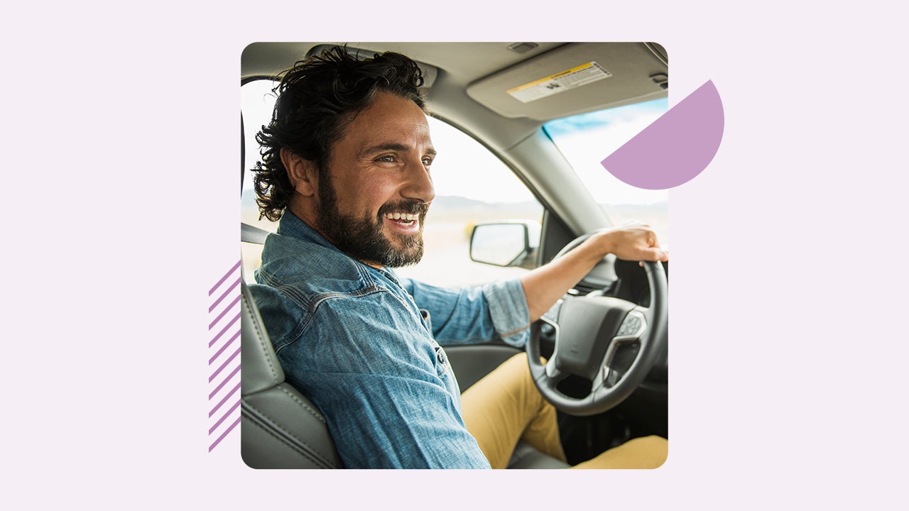 A smiling white man sits in the driver's seat of a car.
