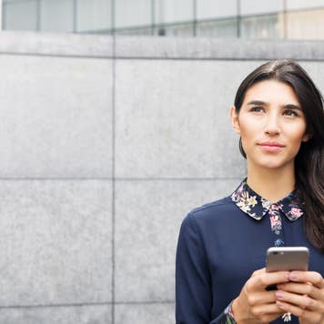 A woman holding a phone looks pensively into the distance.