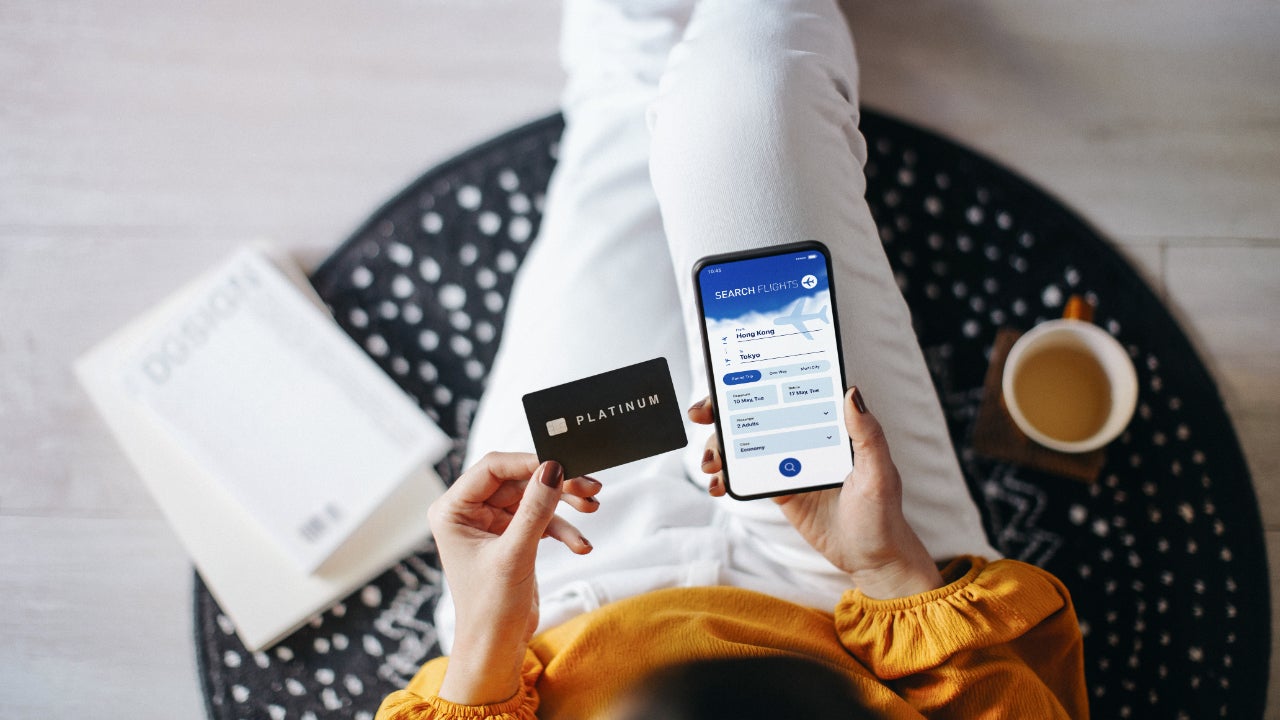 Woman booking flight tickets on airline website online with smartphone and making payment with credit card at home