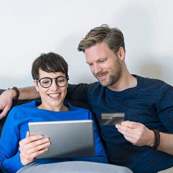 Happy casual couple relaxing on couch using tablet and holding credit card