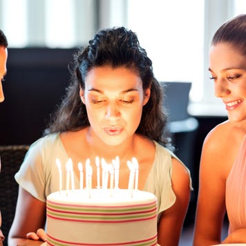 Young woman blowing birthday candles while friends looking at it in restaurant. Horizontal shot.