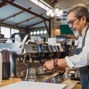 A coffeeshop owner uses his coffee machine at bar counter in cafe.