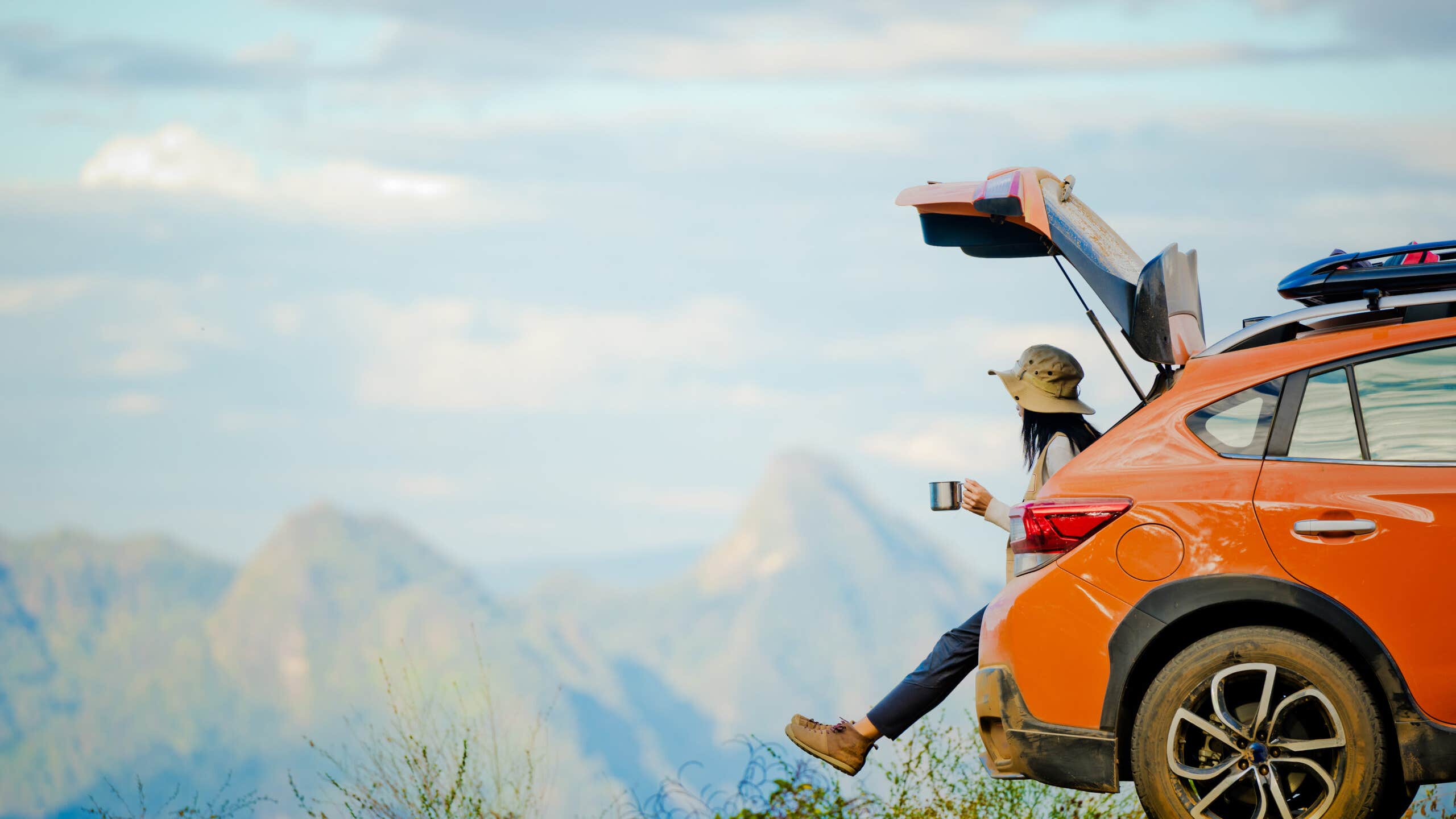 Female traveler enjoying the scenic view on the peak of mountain while sipping coffee