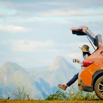 Female traveler enjoying the scenic view on the peak of mountain while sipping coffee