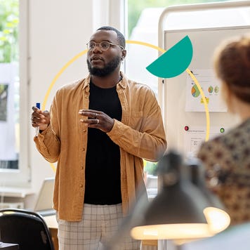 A man speaks with coworkers in front of a whiteboard.