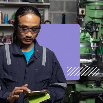 A black man wearing coverals uses a cell phone in a small business.