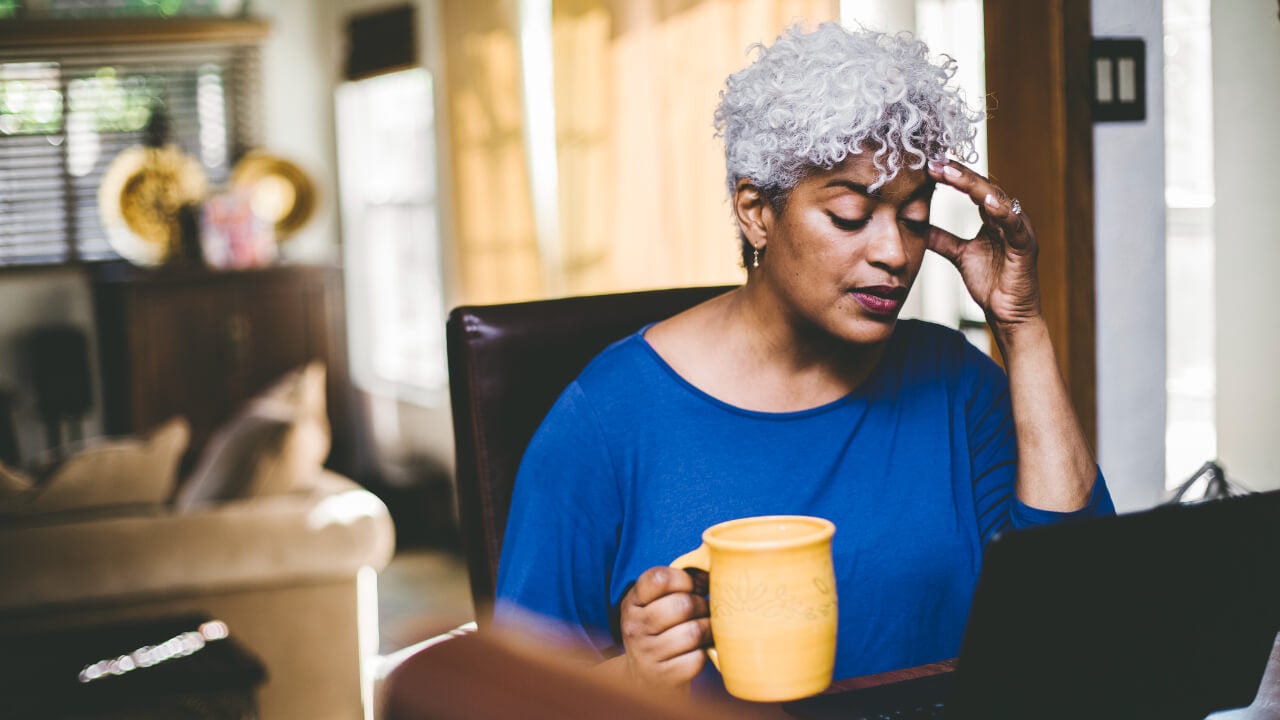 A woman with white hair puts a hand to her forehead while focusing on a computer screen.