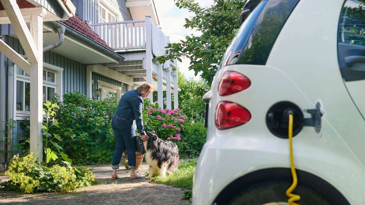 Woman walking to entrance of her house while her electric car is charging