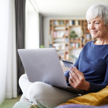 Senior woman using credit card while doing online shopping on laptop at home