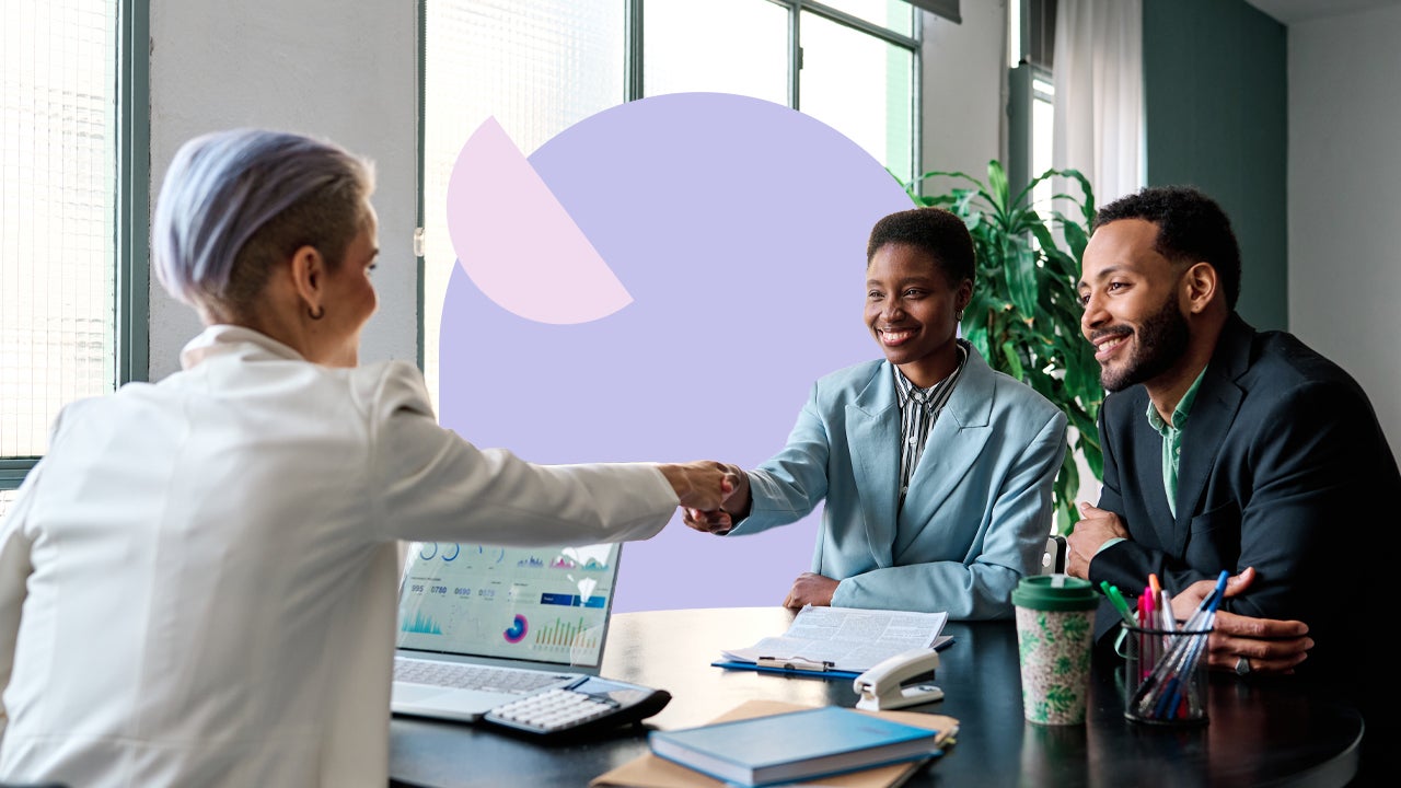 A Black business woman and her business partner shake hands across a table with another businessperson.