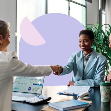 A Black business woman and her business partner shake hands across a table with another businessperson.