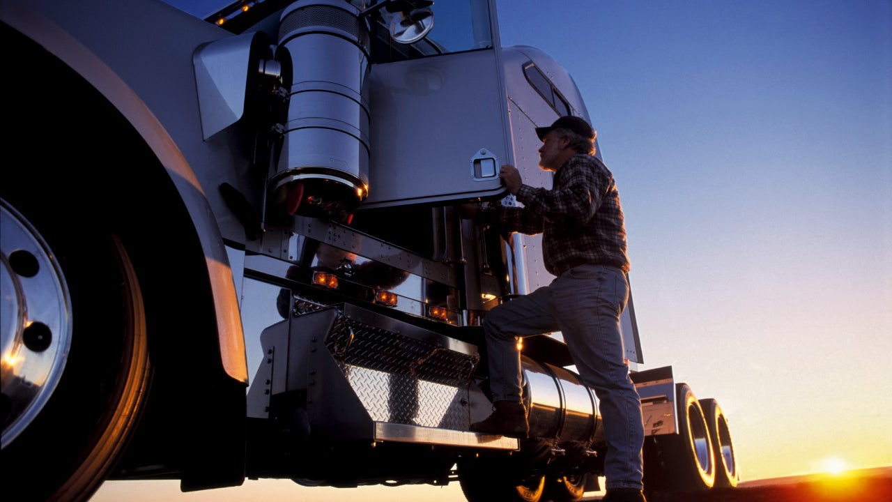 A truck driver getting into his semi truck at dawn.