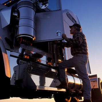 A truck driver getting into his semi truck at dawn.