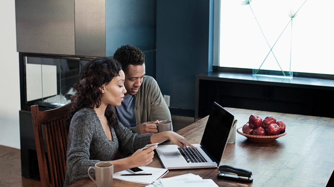 Woman using laptop while husband drinks coffee