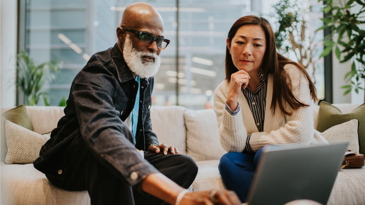 A man and a woman on a stylish white sofa in a contemporary office building have a casual business meeting