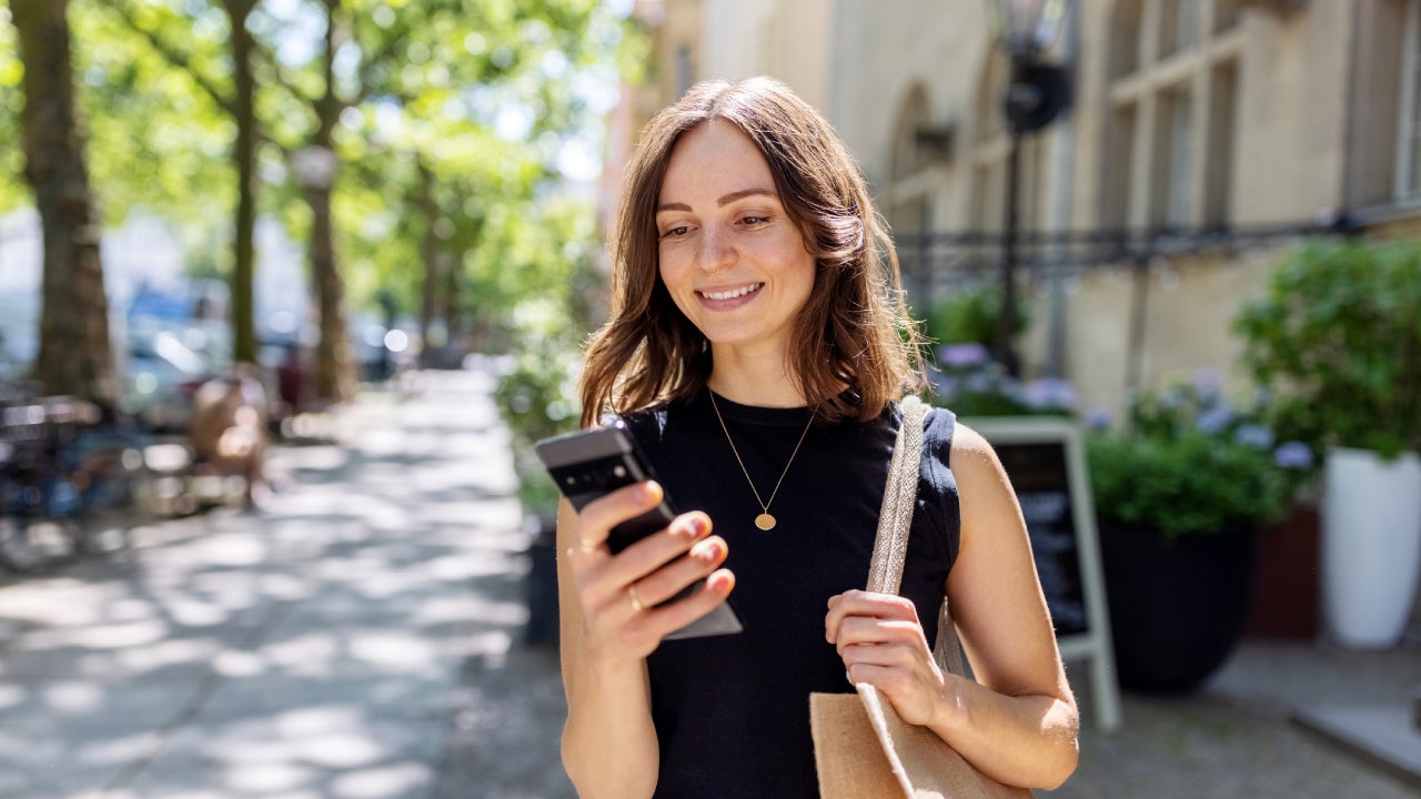 Smiling person with smartphone walking on the street