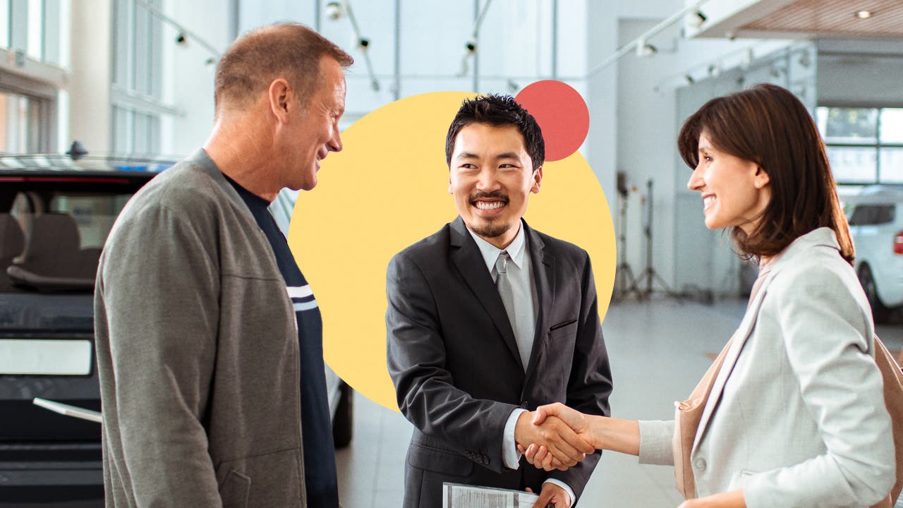 A couple at a car dealership shaking hands after settling on an offer.