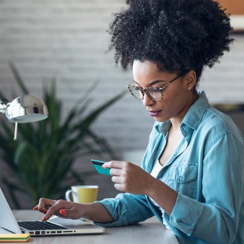 Pretty young afro woman shopping online with credit card with laptop while working on office at home.