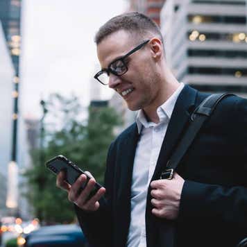 Man smiling at his cell phone in a busy downtown area