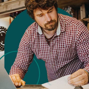 Man reviewing paperwork in front of a laptop in his workshop.