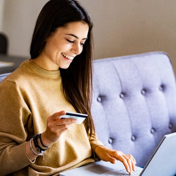 Young woman with credit card shopping over laptop while sitting at home