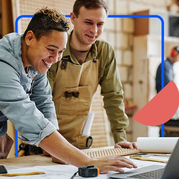 Two carpenters in their shop look at their laptop.